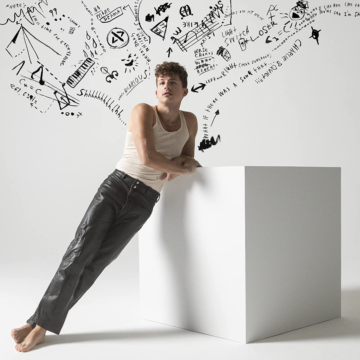 Charlie Puth leaning against a white cube with black doodles on a white background.