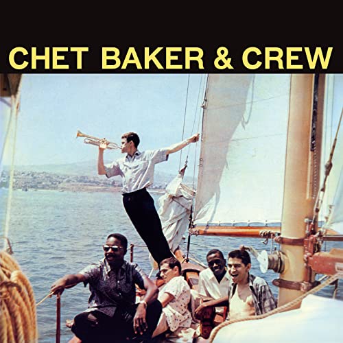 Chet Baker playing trumpet on a sailboat with a crew below.