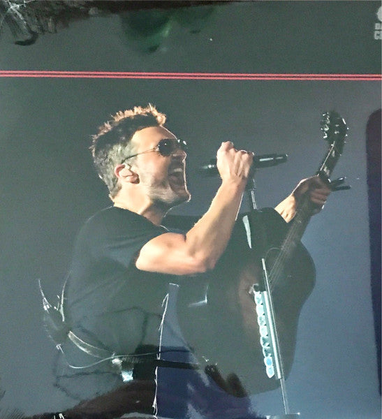 Man in sunglasses singing into microphone while holding guitar.