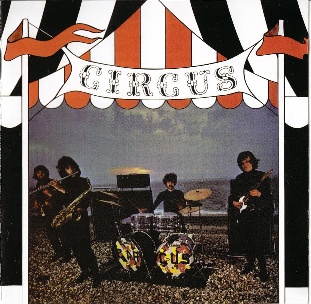 Album cover for "Circus" featuring a band on a beach, under a circus tent.