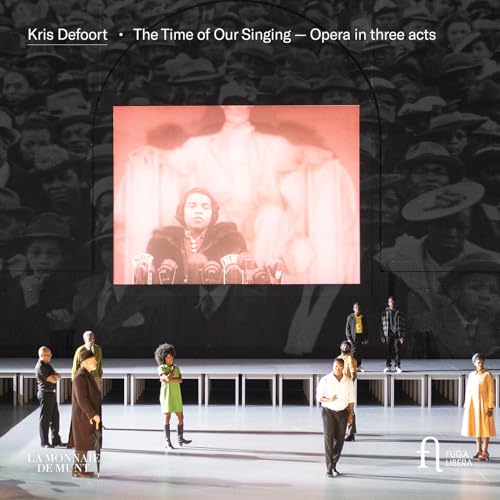 Opera stage with performers and a large projected image of a man with microphones.