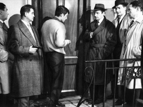 Black and white film still of men in coats, one holding a gun.
