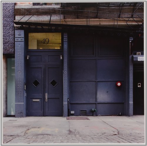 The image shows a black double door with a large garage door beside it. For accessibility purposes, a concise descriptive alt text could be: "Black double door with diamond-shaped windows and adjacent large garage door."