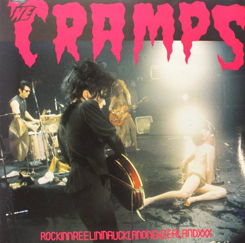 The Cramps performing live on stage with bright pink text on a black background.