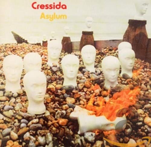 Album cover: white mannequin heads amidst stones and burning objects.