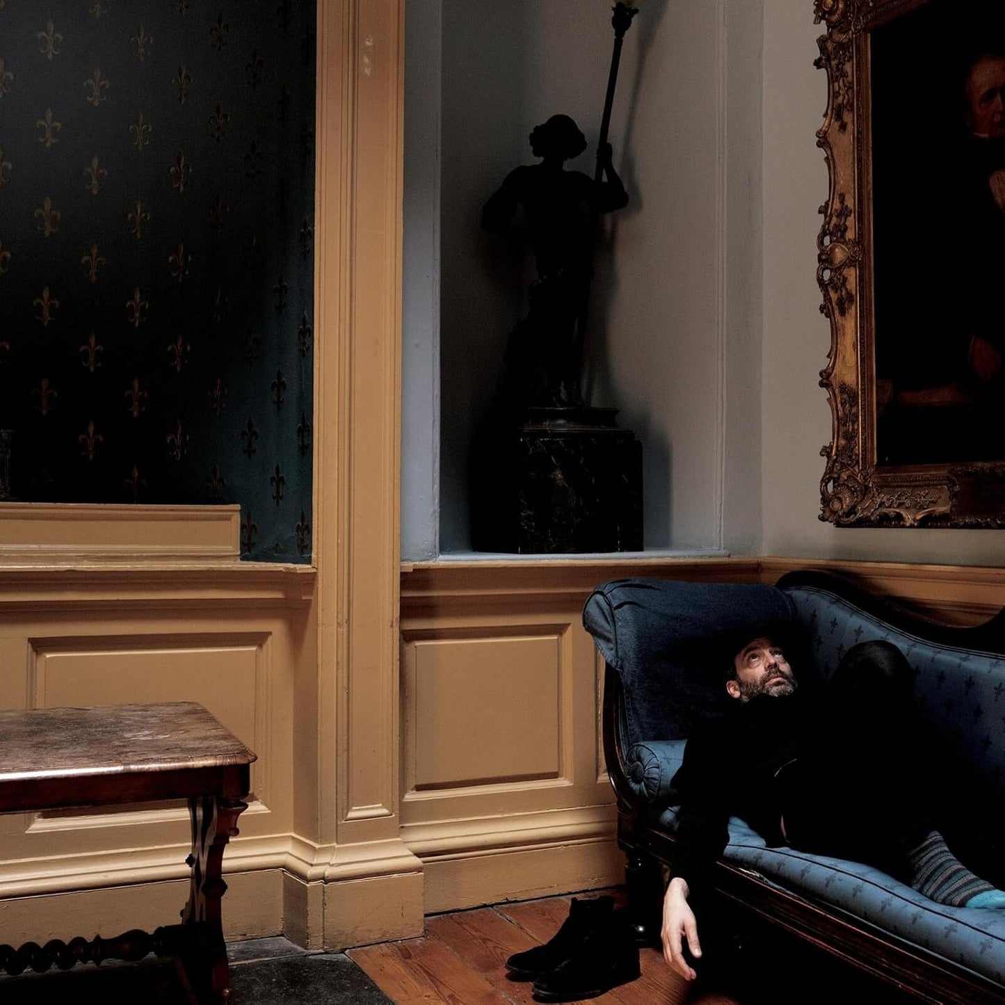 CD cover: man reclining on a sofa in a decorated room.