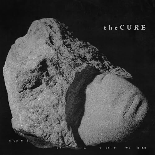 The Cure album cover: a dark, textured rock with a face-like form.