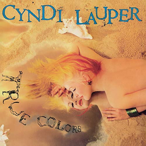 Cyndi Lauper lying on sand with her reflection visible in a pool of water.