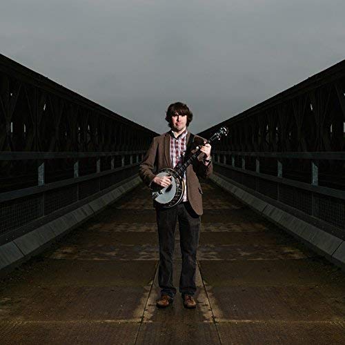 Dan Walsh holding a banjo on a metal railway bridge.