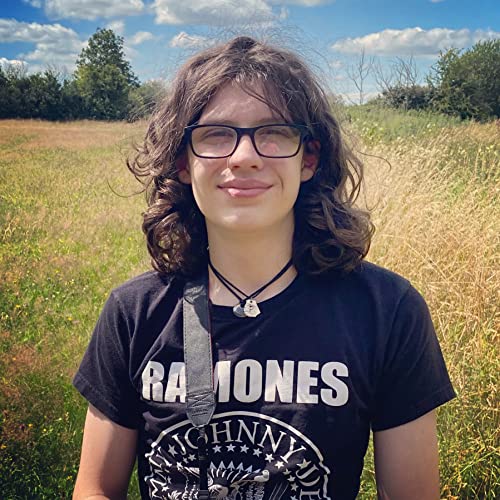 Young person with curly hair in a field, wearing a Ramones t-shirt.
