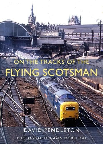 A blue and yellow diesel locomotive travels on tracks toward a large city station.