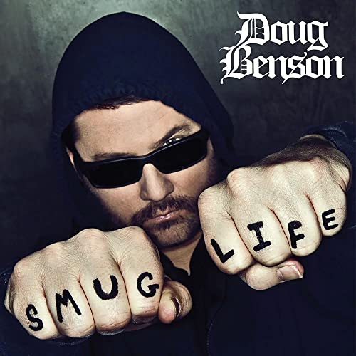 Doug Benson wearing a hood and sunglasses with SMUG LIFE tattooed on his knuckles.