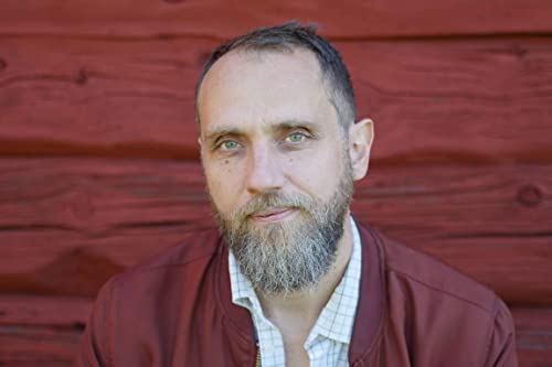 Headshot of a man with a beard against a red wooden wall.