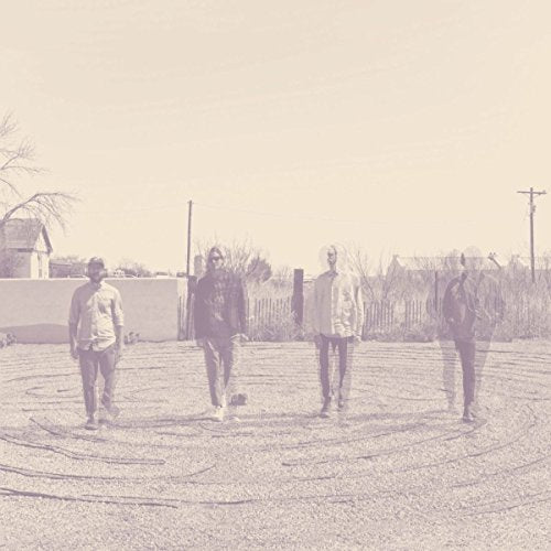 Four men standing in a circle on a gravel surface, monochromatic image.