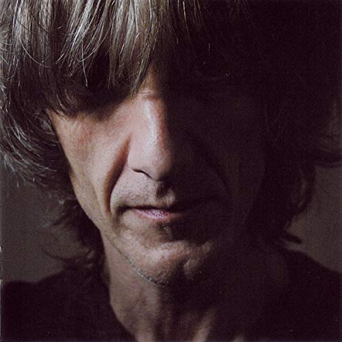 Close-up portrait of a man with long hair, partially obscured in shadow.