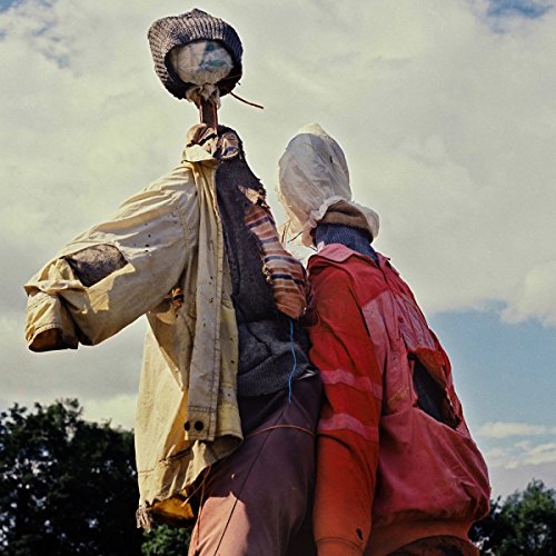 Two figures in draped clothing stand against a cloudy sky.