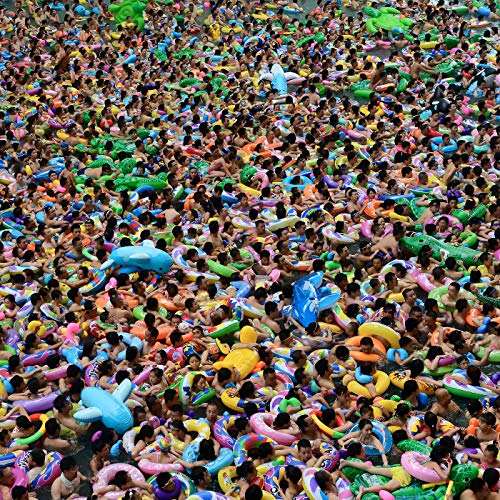 Crowded swimming pool filled with people and colorful inflatable toys.