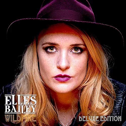 Close-up portrait of Elles Bailey wearing a dark hat against a black background.