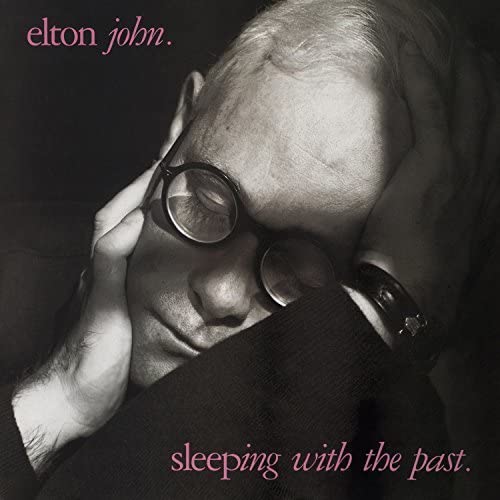 Black and white portrait of Elton John wearing sunglasses, album cover.