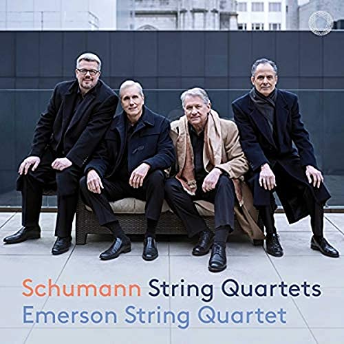 Four men, the Emerson String Quartet, seated against a gray building.