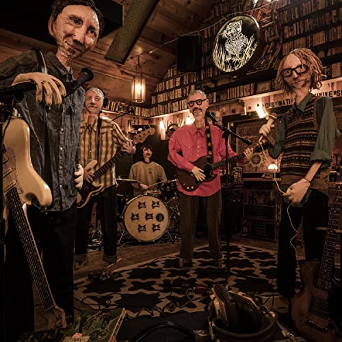 Four musicians in a room with instruments and bookshelves.
