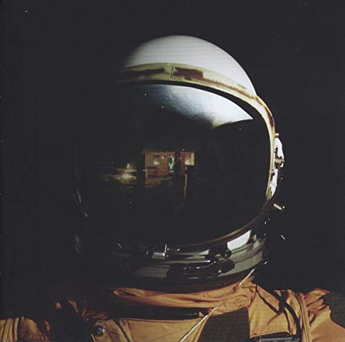 Close-up of an astronaut helmet reflecting a dark, illuminated house against a black background.