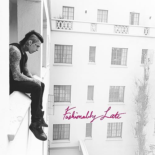 Tattooed man sitting on a ledge of a white building with Fashionably Late text.