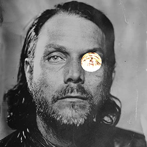 Black and white portrait of a man with a coin over one eye.