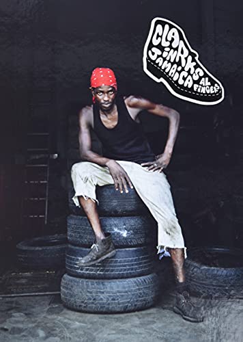 Man wearing Clarks shoes sits on stacked tires in Jamaica.