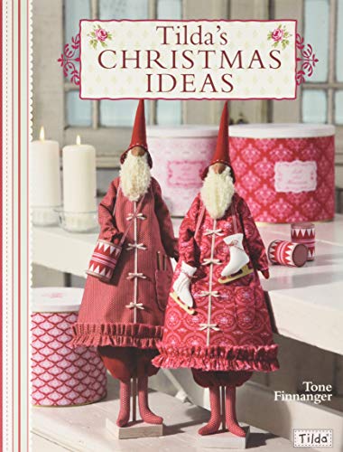 Two fabric Santa dolls in red coats standing on a table with candles.