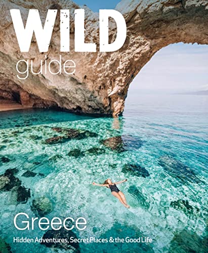 A person floats in clear turquoise water beneath a natural stone arch in Greece.