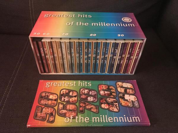 Boxed set of “Greatest Hits of the Millennium” CDs on a dark surface.