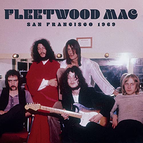Five band members in casual clothes sitting and standing, one holding a guitar.