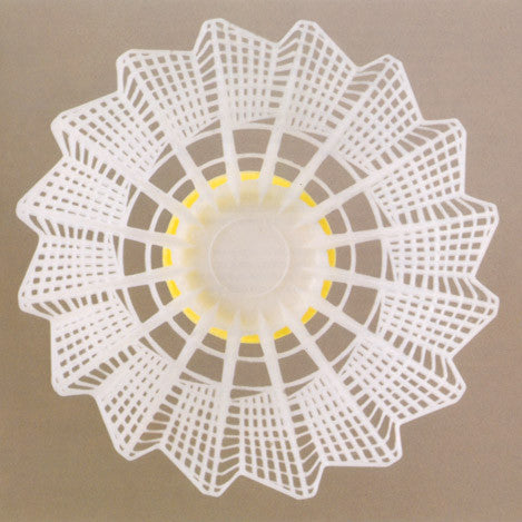 White shuttlecock with yellow base, viewed from above on a tan surface.