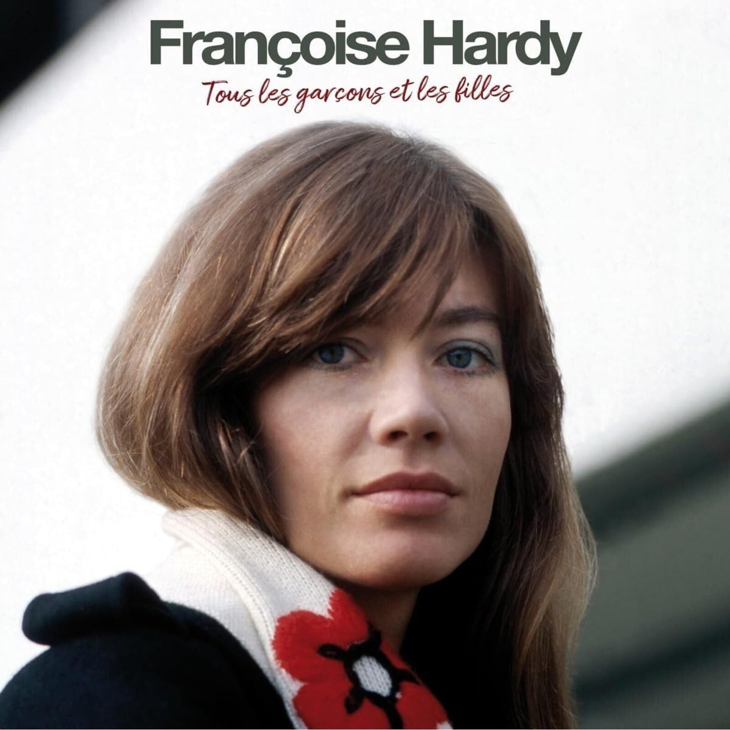 Portrait of Françoise Hardy with brown hair wearing a white scarf with red flowers.