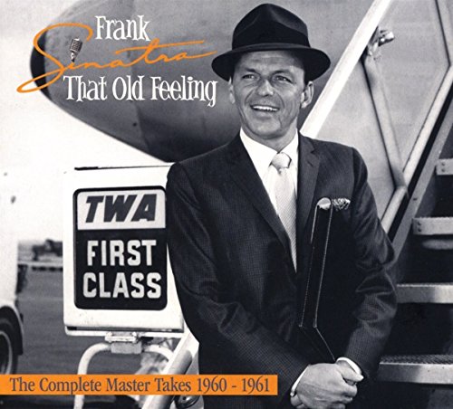 Frank Sinatra wearing a fedora and suit standing by a TWA airplane staircase.