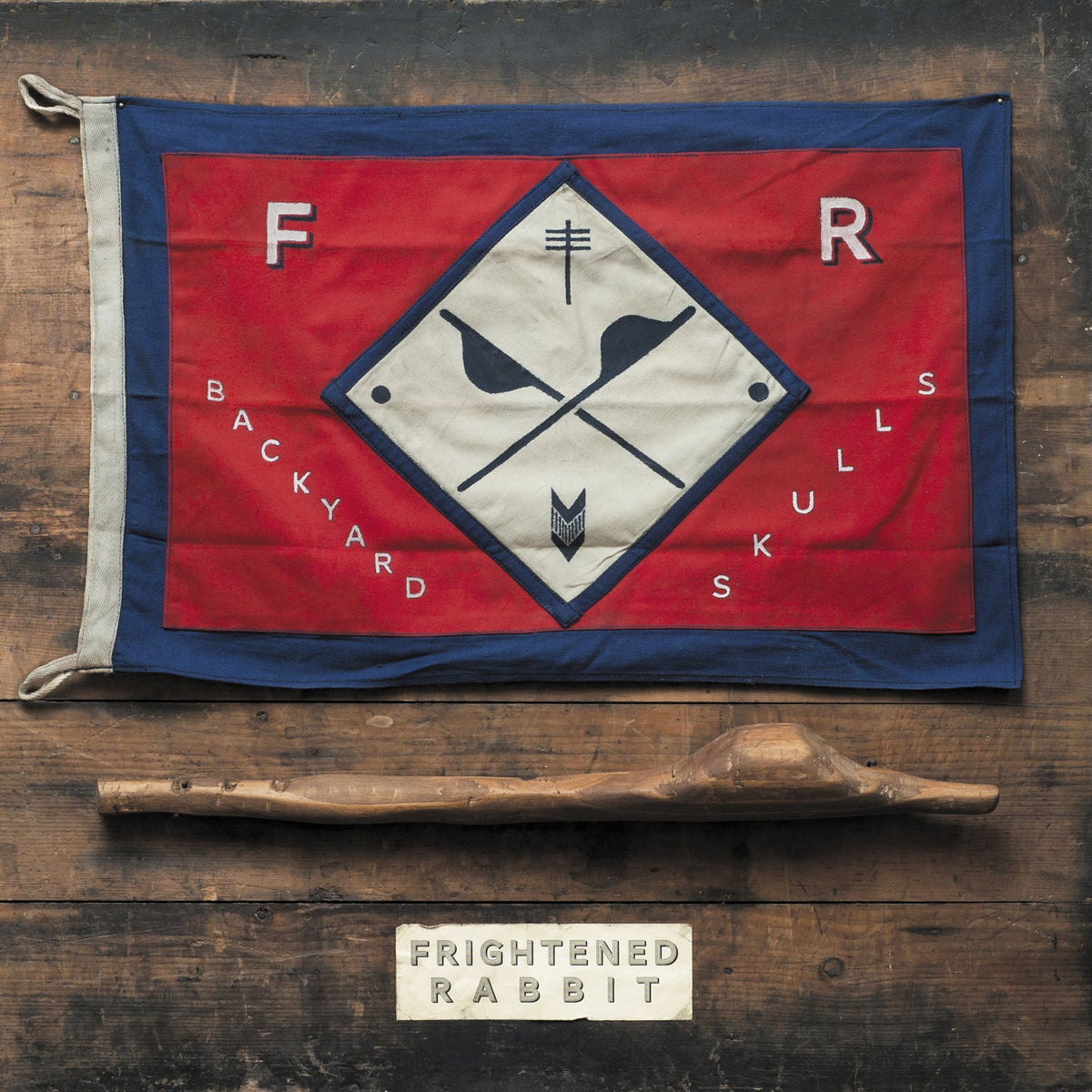 "Red and blue flag with skull design and 'Frightened Rabbit' text on wooden surface."