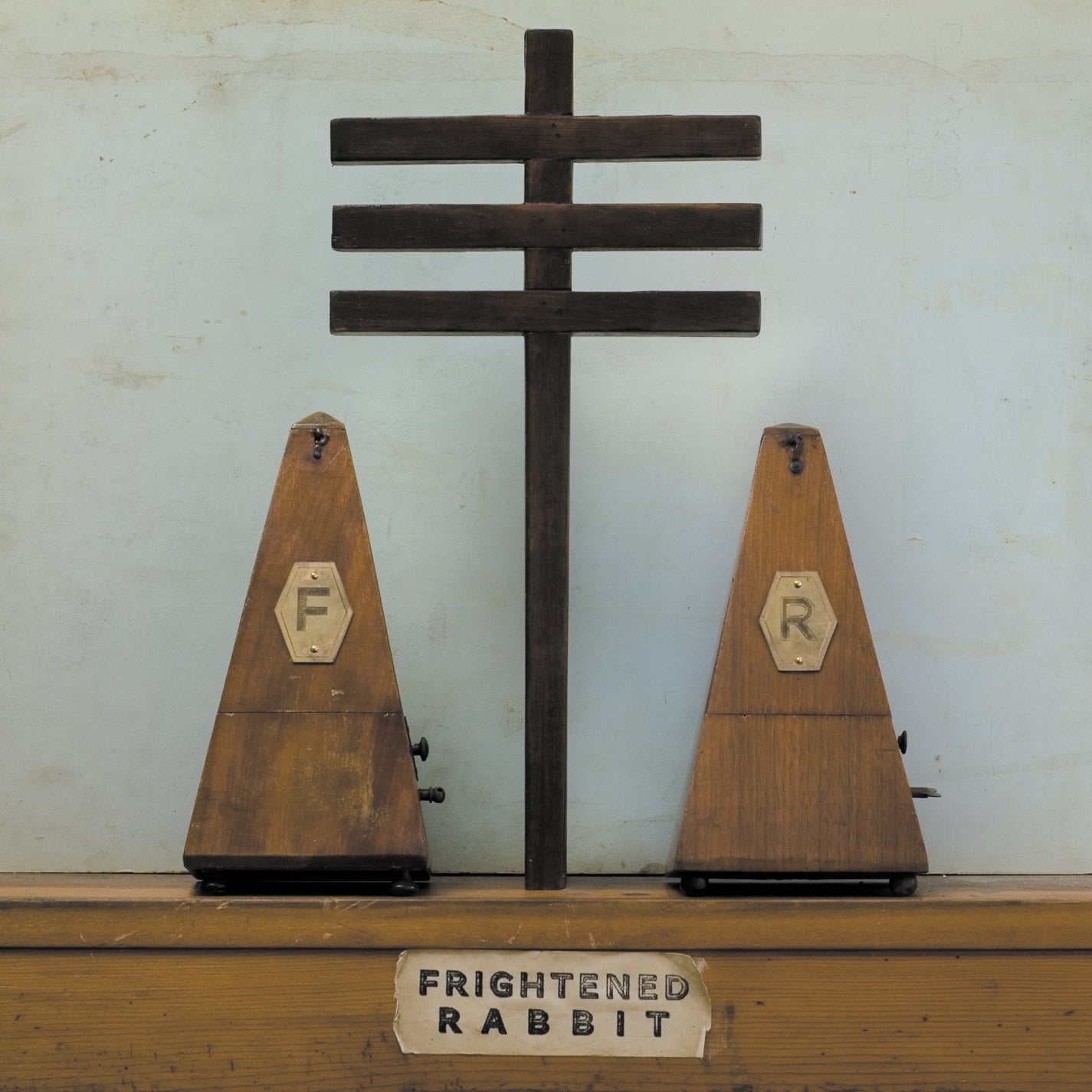 "Two wooden cones labeled 'F' and 'R' with a cross on a shelf."