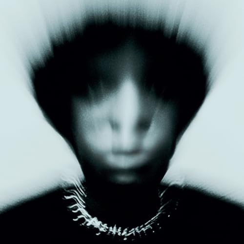 A blurry, motion-effect portrait of a person wearing a necklace against a light background.