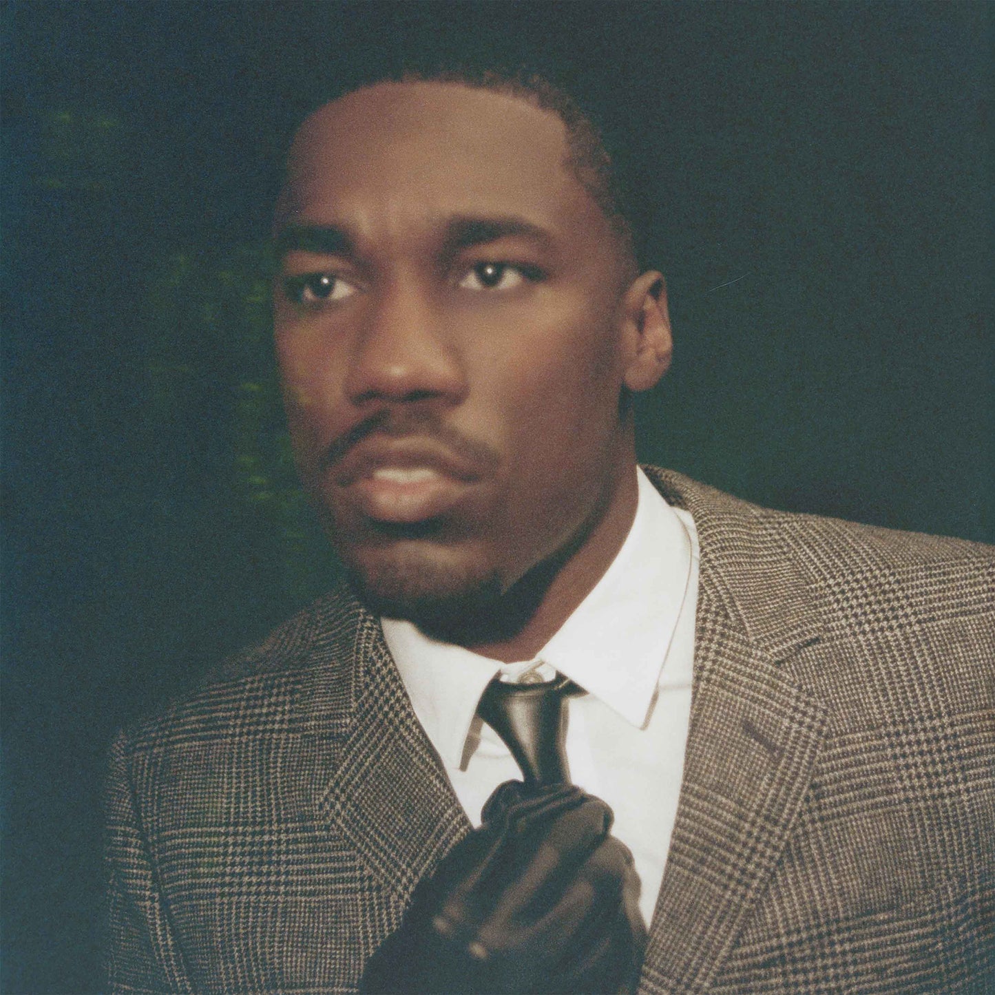 Giveon in a tweed suit, looking directly at the viewer with a serious expression.