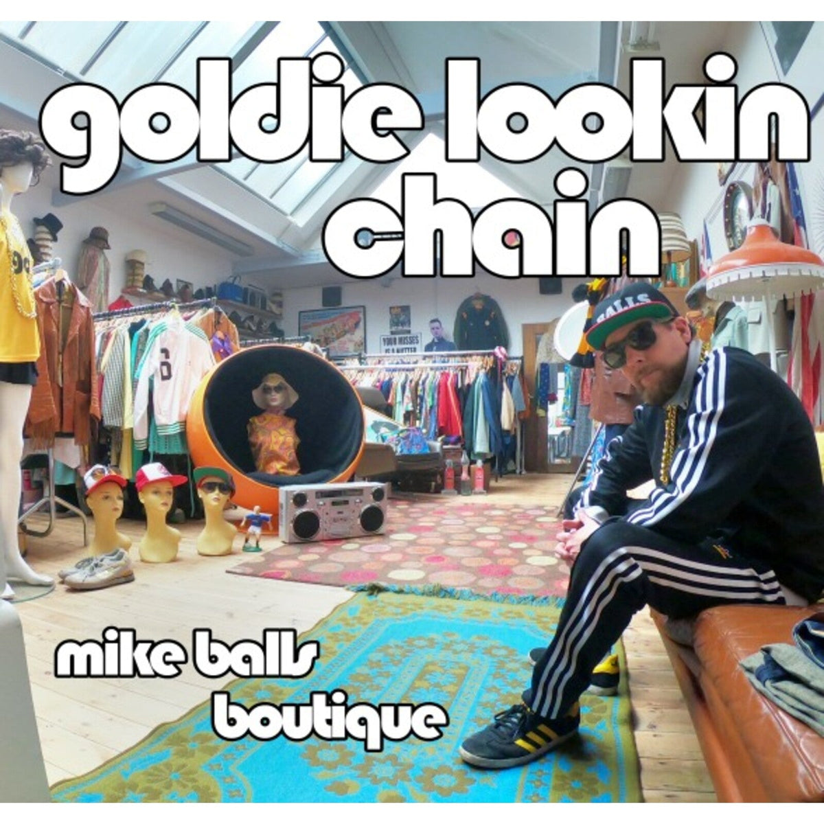 A man in a tracksuit sits in a vintage clothing store with mannequins.