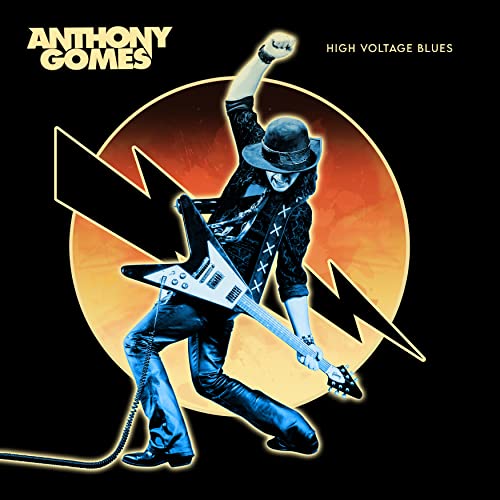 Anthony Gomes playing a black guitar against a yellow and black background.