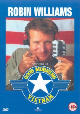 Robin Williams wearing headphones and holding a microphone in front of an American flag.