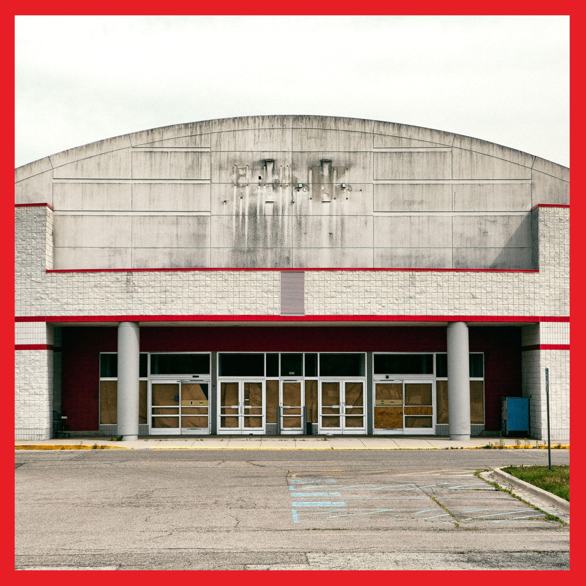 Abandoned, concrete building facade with glass doors and a red border.