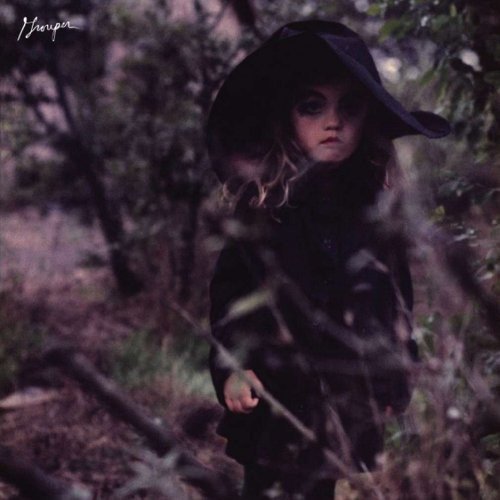 A child in a dark coat and wide-brimmed hat stands in a wooded area.