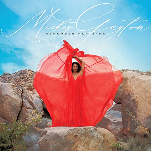 Mickey Guyton album cover: woman in red dress amidst rocky landscape.