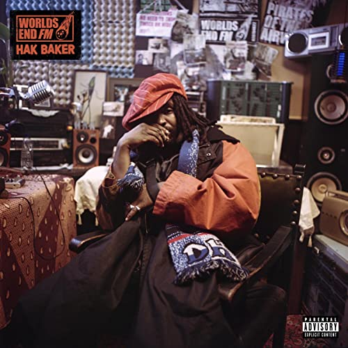 Hak Baker sits in a cluttered recording studio wearing a red hat.