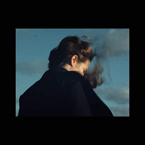 Woman with windswept hair, seen from behind, against a blue sky.