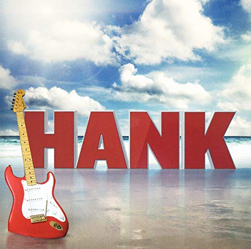 Red electric guitar beside large red letters spelling "HANK" on a beach.