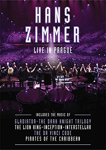 Hans Zimmer performing on stage before a large audience in a purple-lit concert hall.